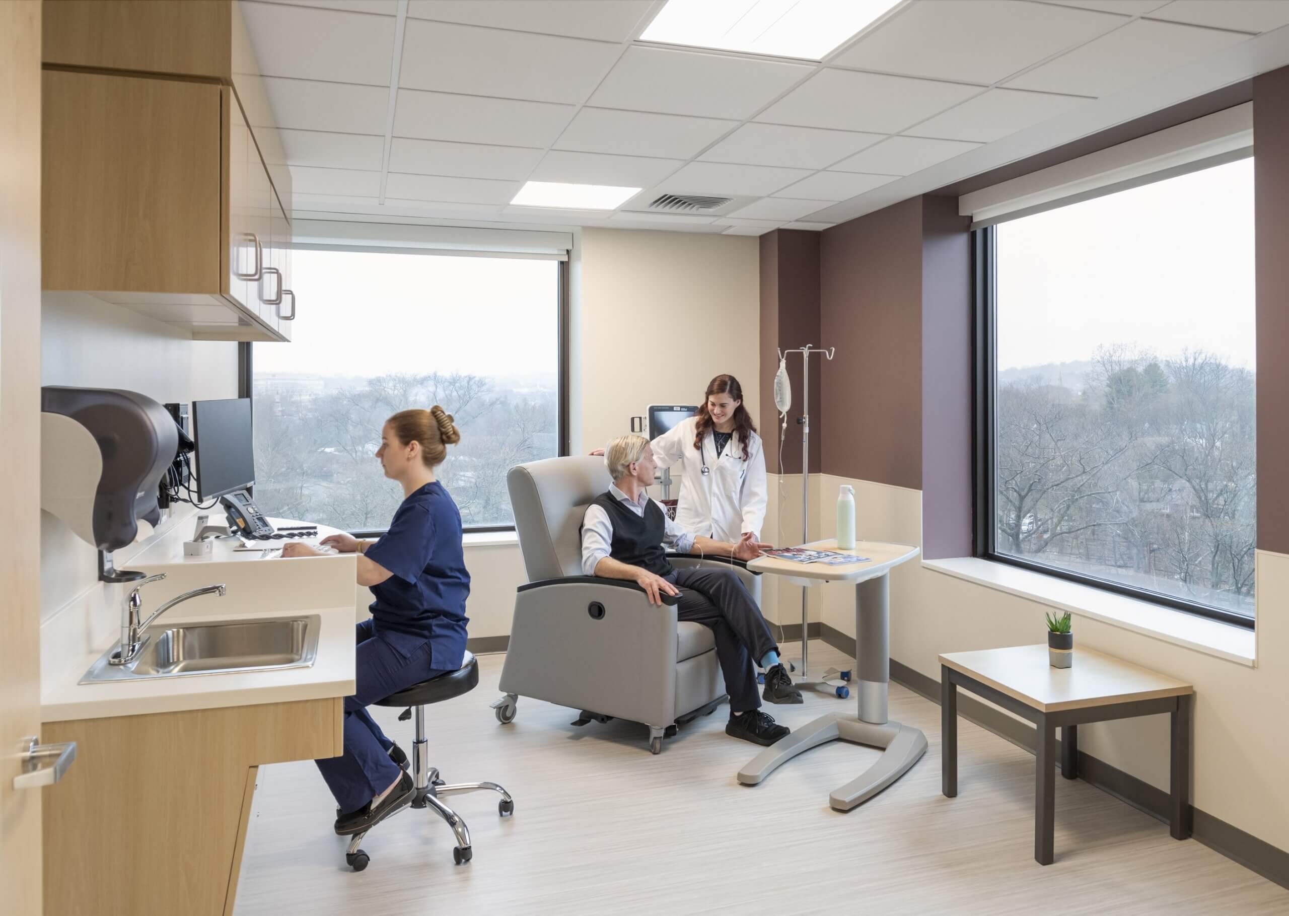 Hospital room where a patient sits in a chair and speaks with a medical professional