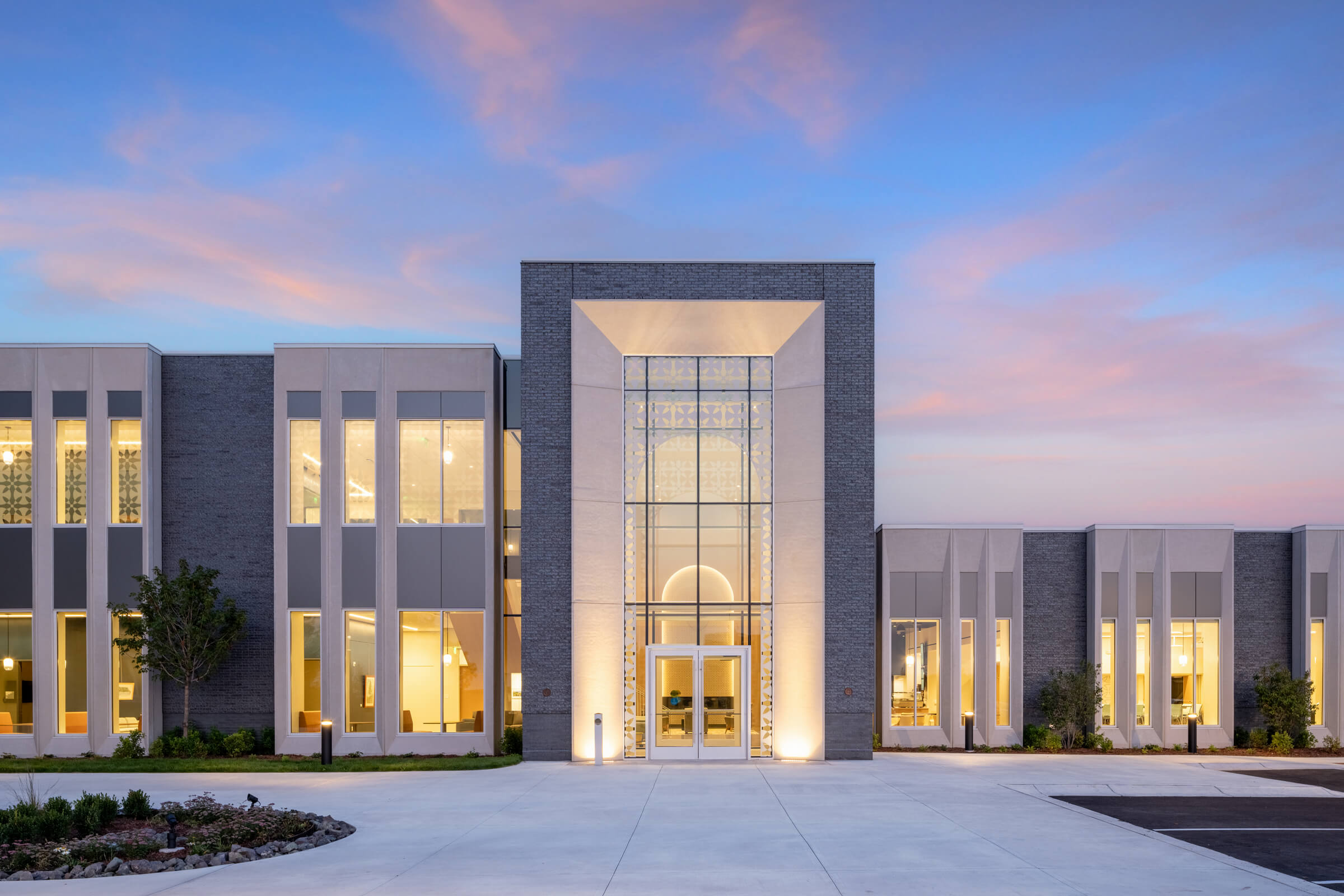 Modern building at twilight with illuminated windows and a grand entrance.