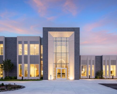 Modern building at twilight with illuminated windows and a grand entrance.