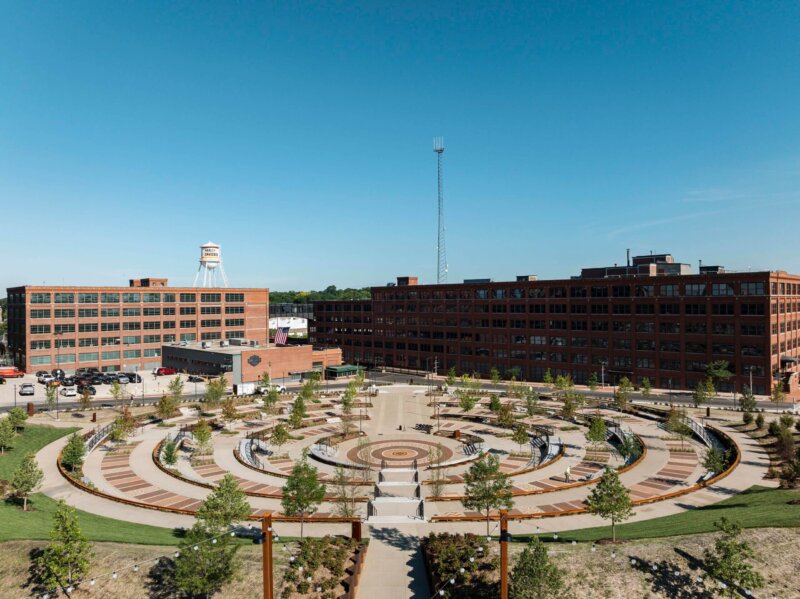 View of Davidson Park with its distinctive industrial structures, featuring a large, circular, terraced garden and surrounded by red brick buildings under a clear blue sky.