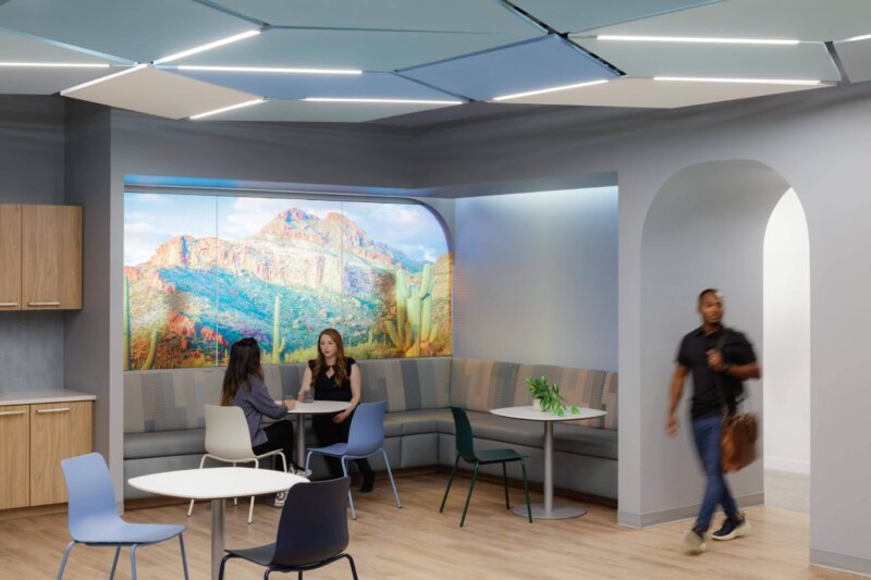 Office lounge area where employees chat in front of a Southwestern mural